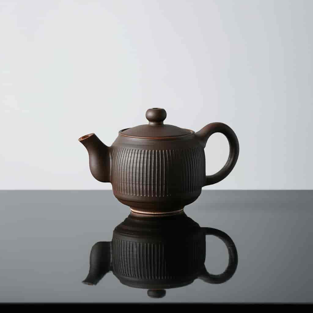High-resolution product photography of a matte ceramic teapot on a reflective black surface with dra