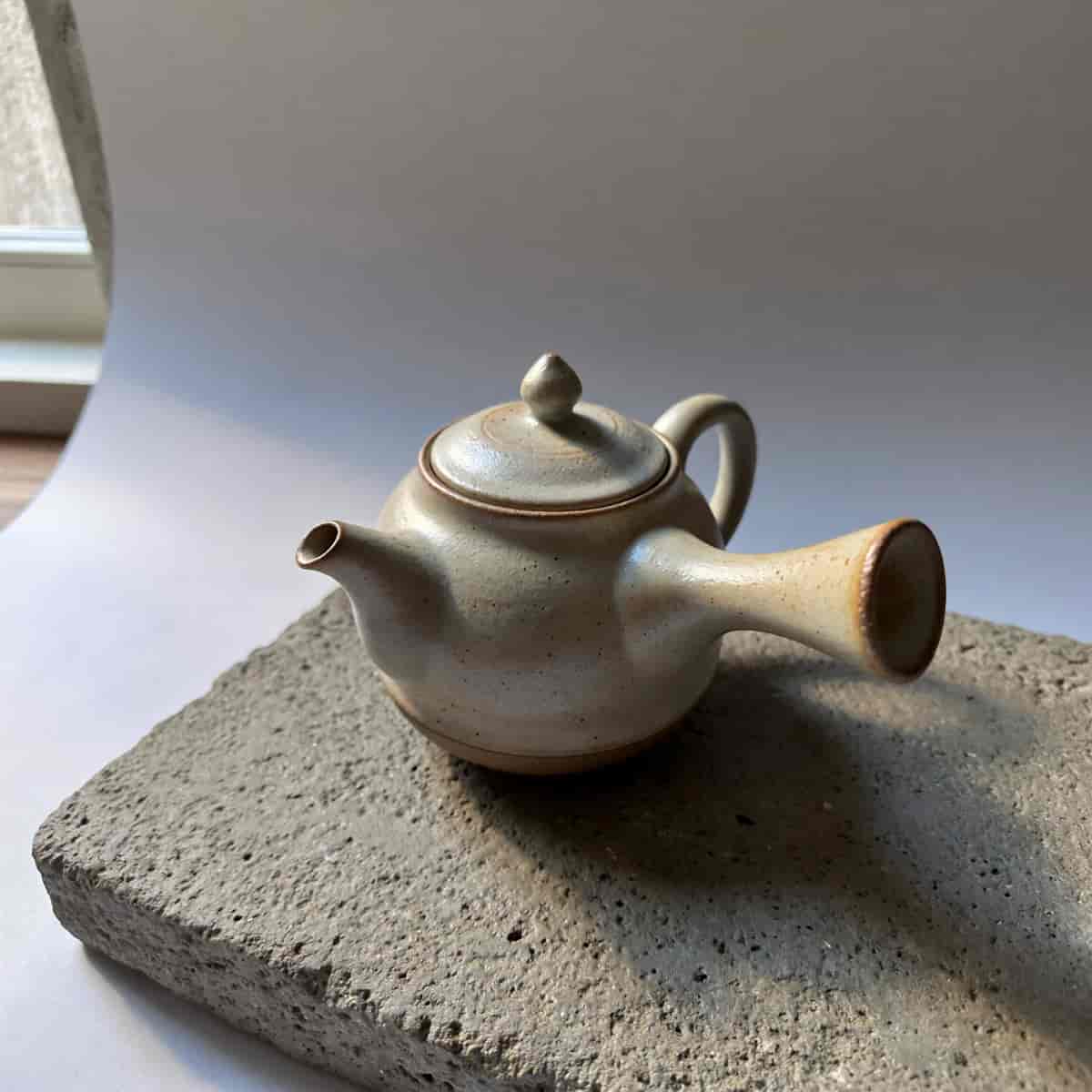 Minimalist product photography of a hand-thrown ceramic teapot on a textured concrete slab, soft dif